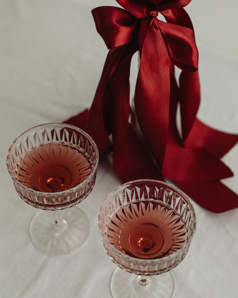 two glasses of red wine on white tablecloth with candlestick and red satin ribbon bow